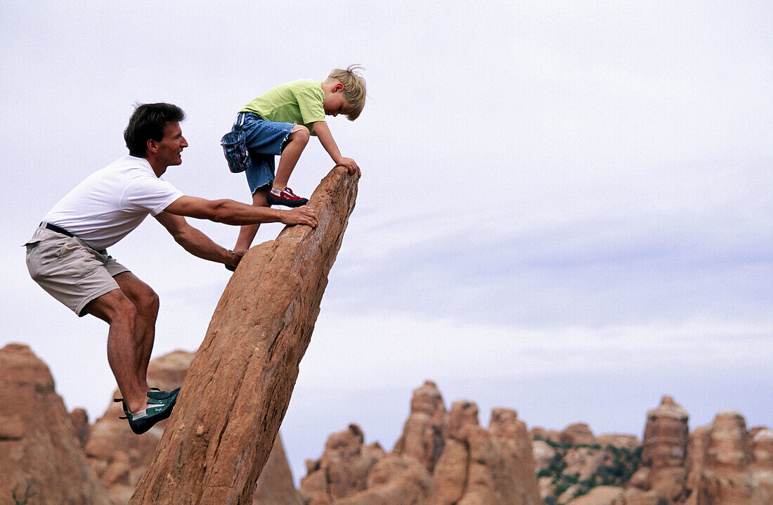 Father and son climbing a sandstone slab. Utah. USA