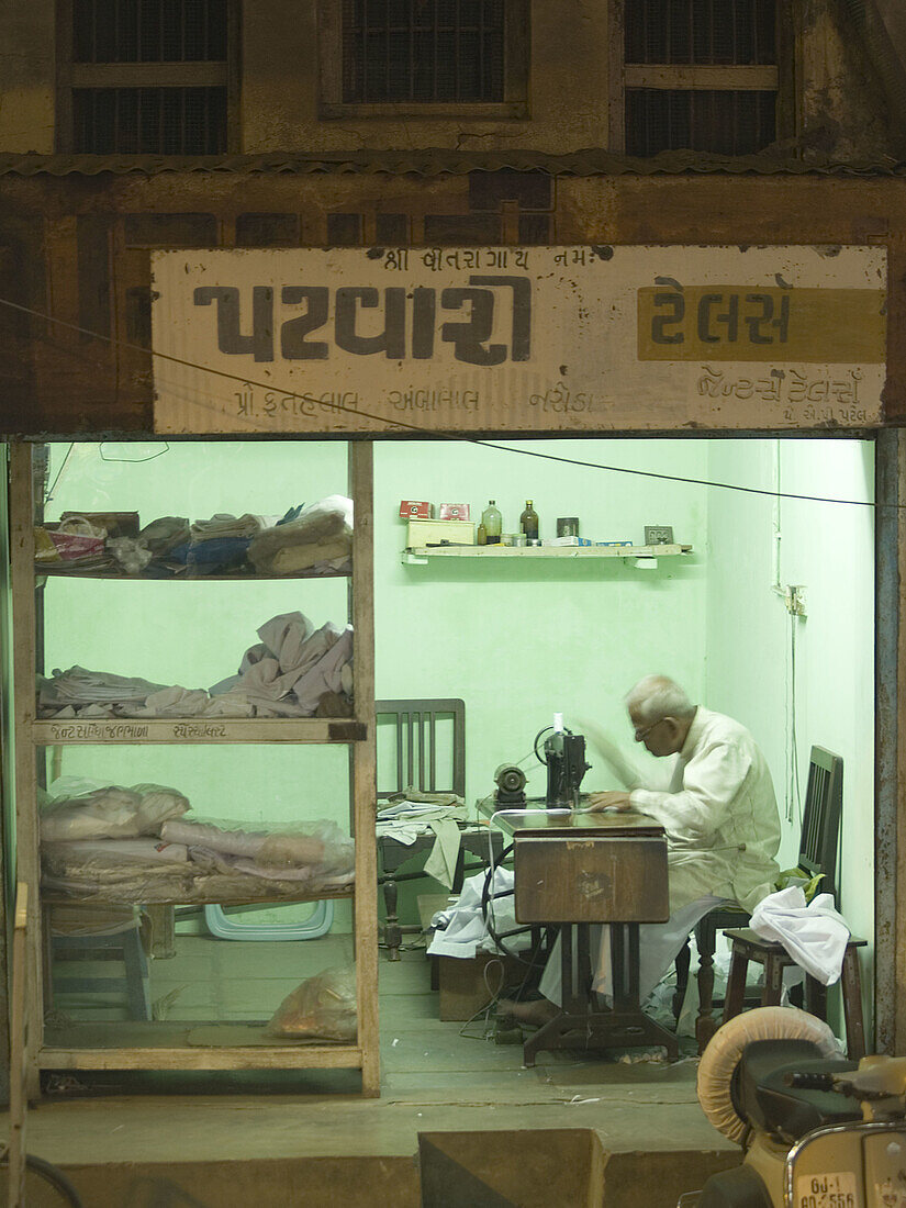 Tailor at work at night in his shop in Naroda, Gujarat, India