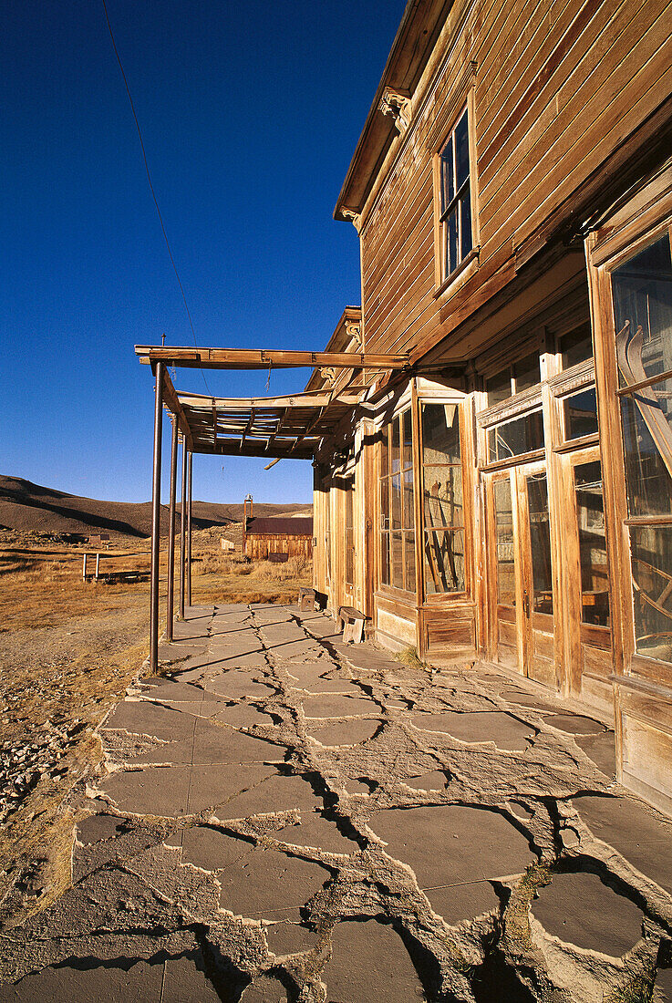 Evening light on cracked sidewalk and the front of the Wheaton and Hollis Hotel on Main Street, Bodie State Historic Park (National Historic Landmark), California