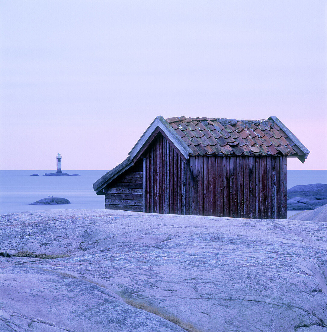 Small old hut at remote location by the coast with lighthouse in background. The Bohus Archipelago. Sweden.