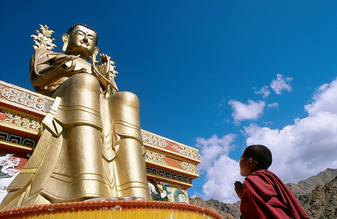 Novice monk praying in front of a giant buddha at Likkir Monastery. Ladakh. Jammu and Kashmir, India