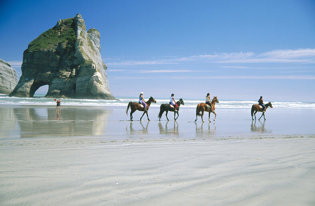 Group of horse riders on Wharariki beach with the Archway island behind Farewell spit, Golden Bay.