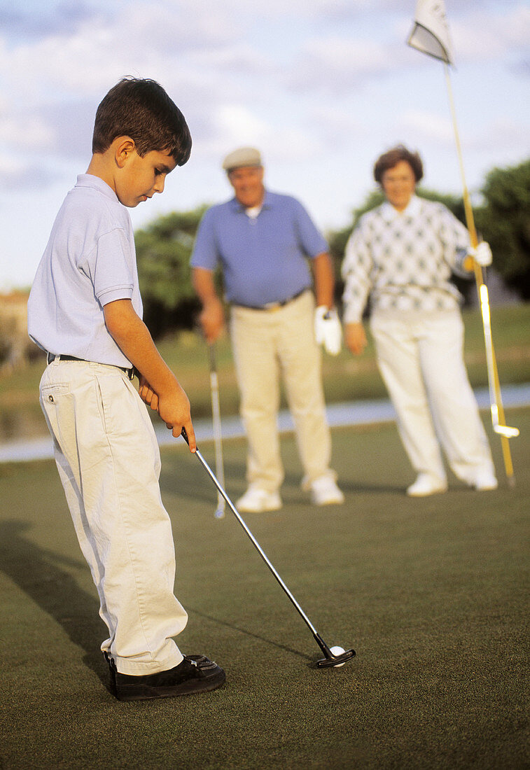 Boy playing golf with his grandparents