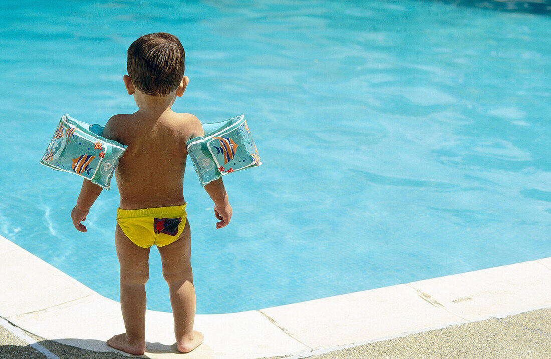 Infant boy standing by a pool