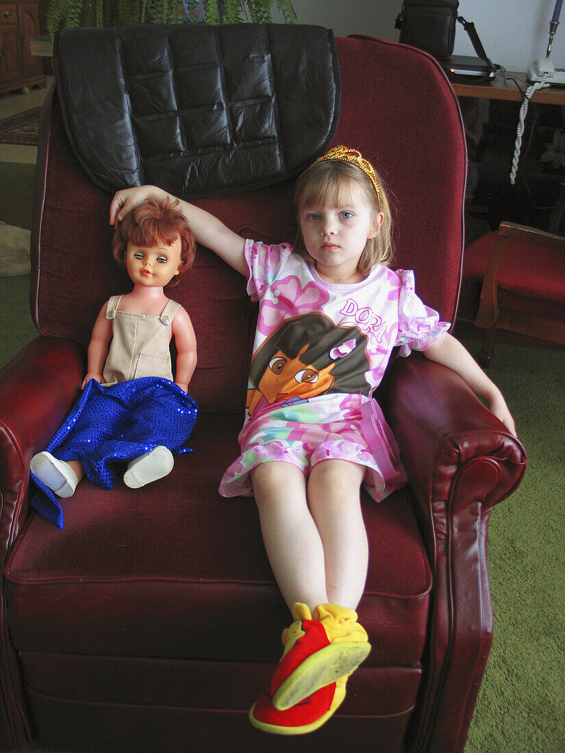 A three year girl with a dolly sits in her grandfather s chair during a visit.