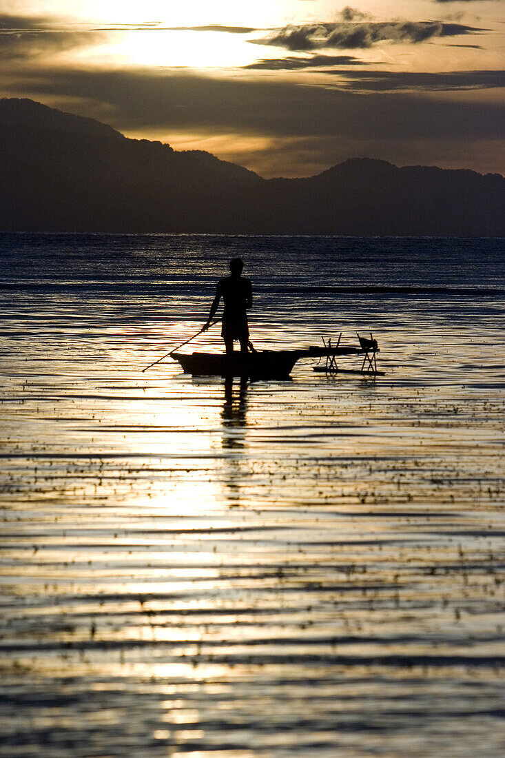 Man standing paddling in a canoo at sunset, New Britain, Papua New Guinea, Oceania