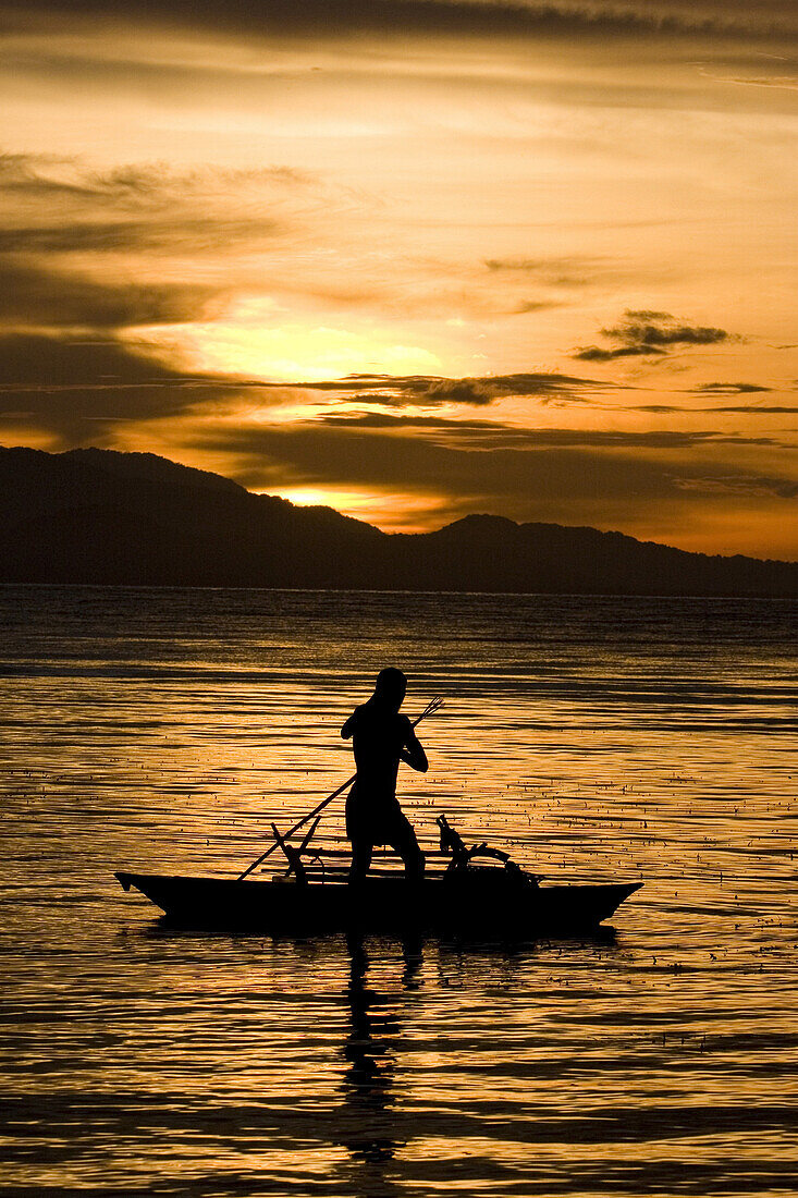 Mann paddelt stehend im Kanu bei Sonnenuntergang, Neubritannien, Papua Neuguinea, Ozeanien