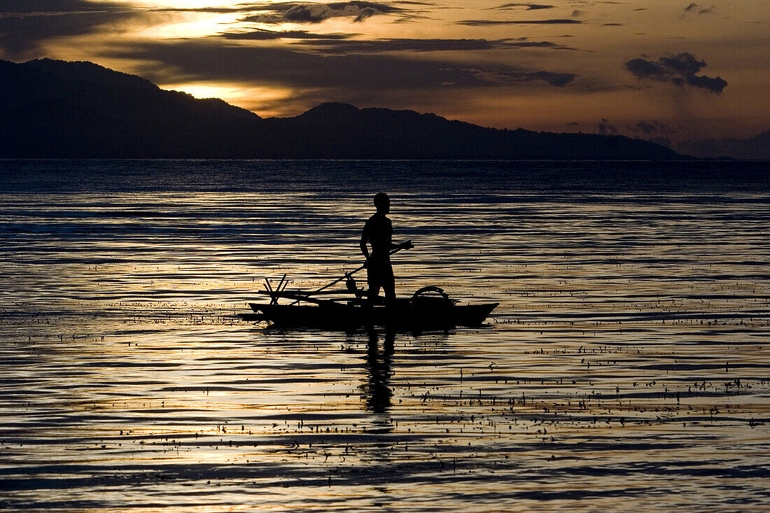 Mann paddelt stehend im Kanu bei Sonnenuntergang, Neubritannien, Papua Neuguinea, Ozeanien