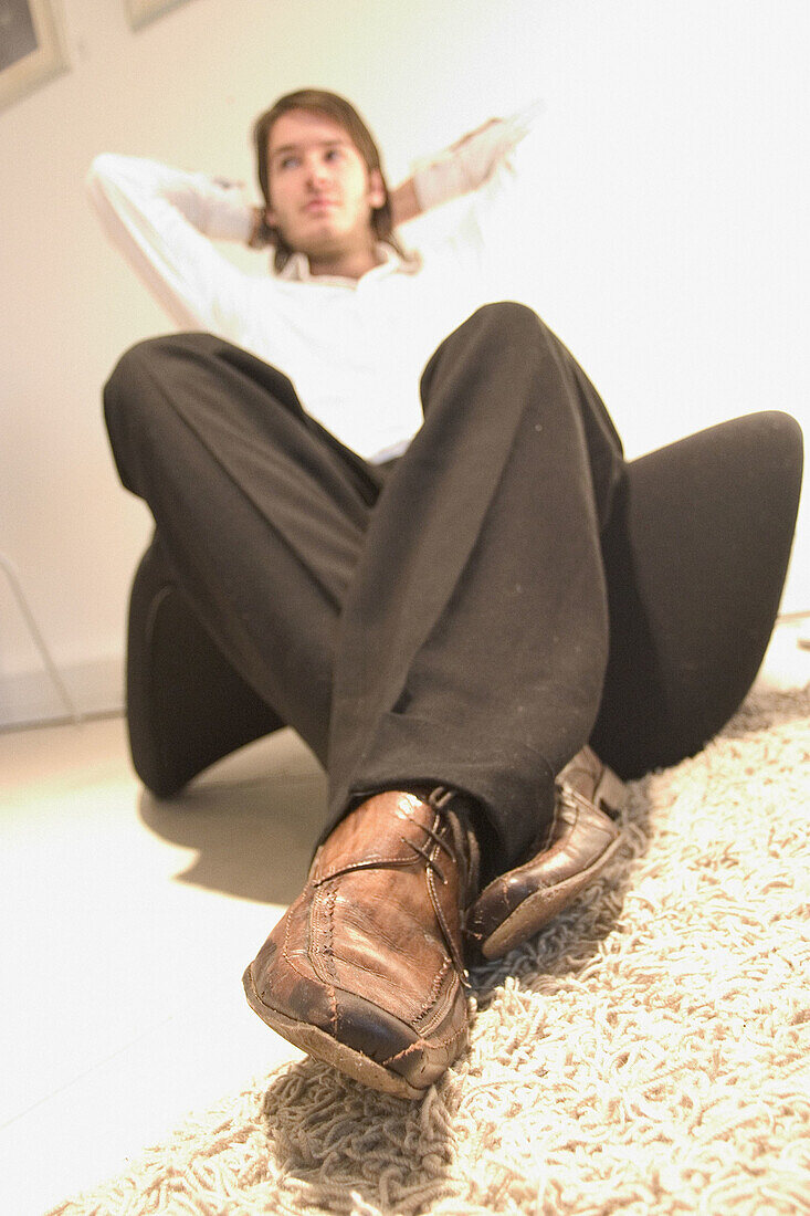 Selective focus on shoes, man sitting on chair with arms behind his head