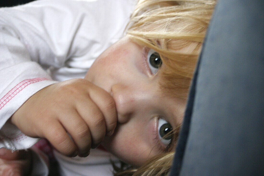 Headshot of a 3 year old girl lying down sucking her thumb, looking into camera