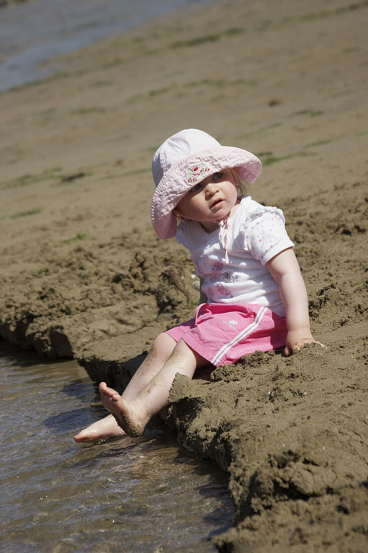 18 month old girl sitting on the beach paddling her feet in the water