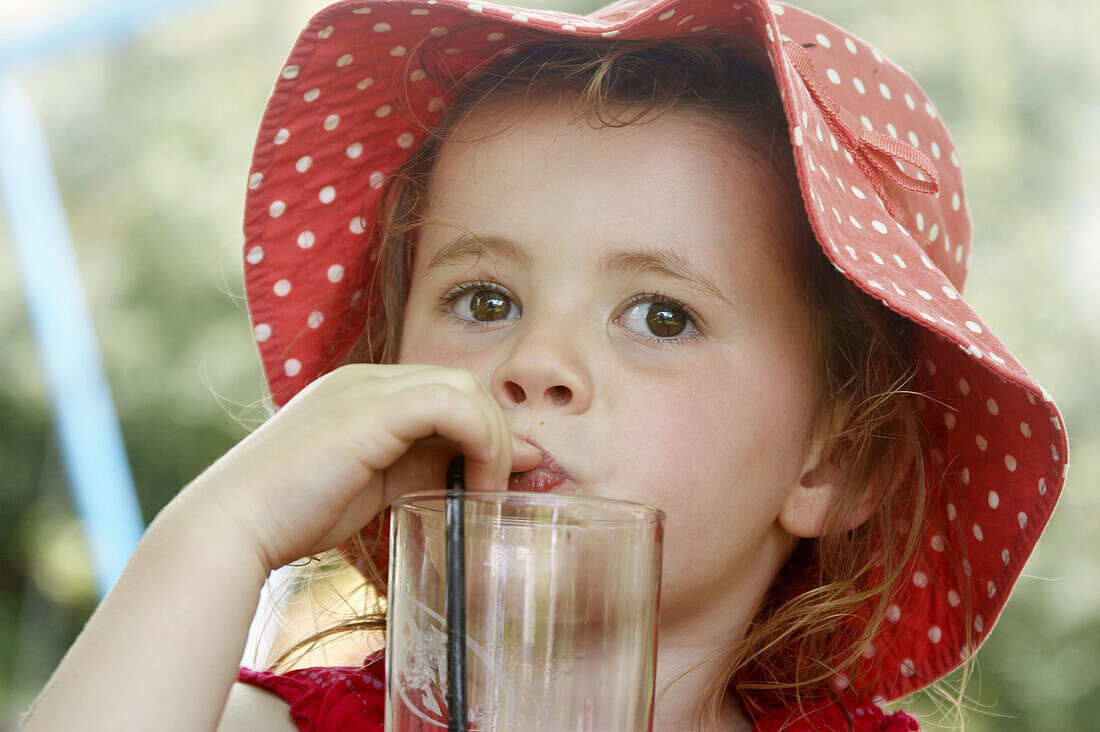 3 year old girl in a big floppy red hat, drinking through a straw