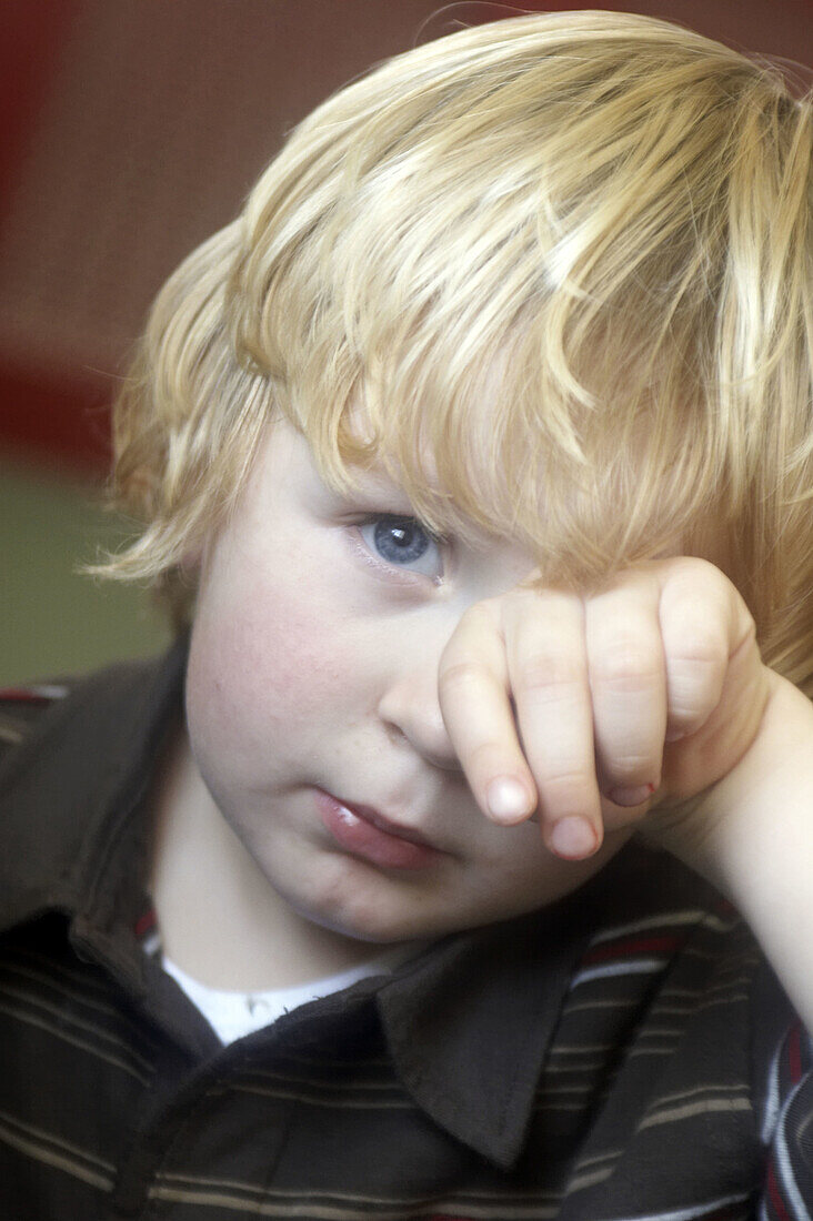 3 year old boy looking into camera at nursery, rubbing one eye