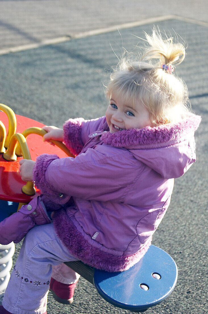 2 year old girl on a rocker in the playground smiling in delight