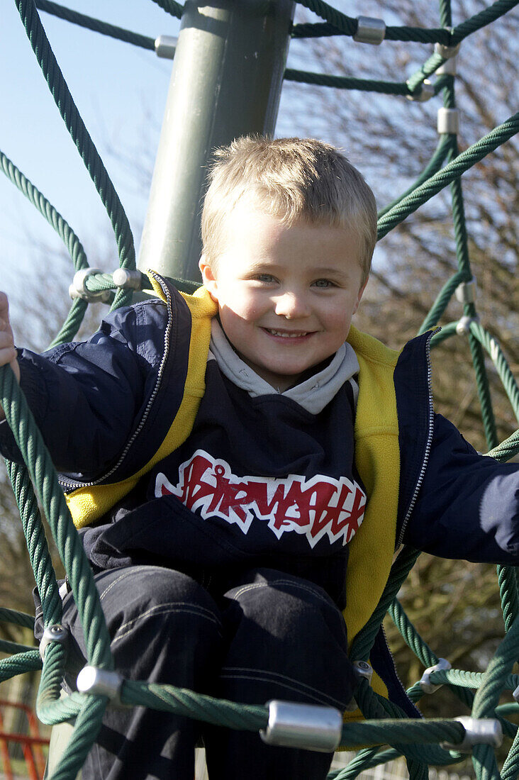 4 year old boy ,on a climbing frame in the park smiling into camera