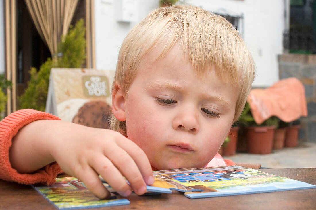 Head of a 2 year old boy as he peers over a table to do a jigsaw.