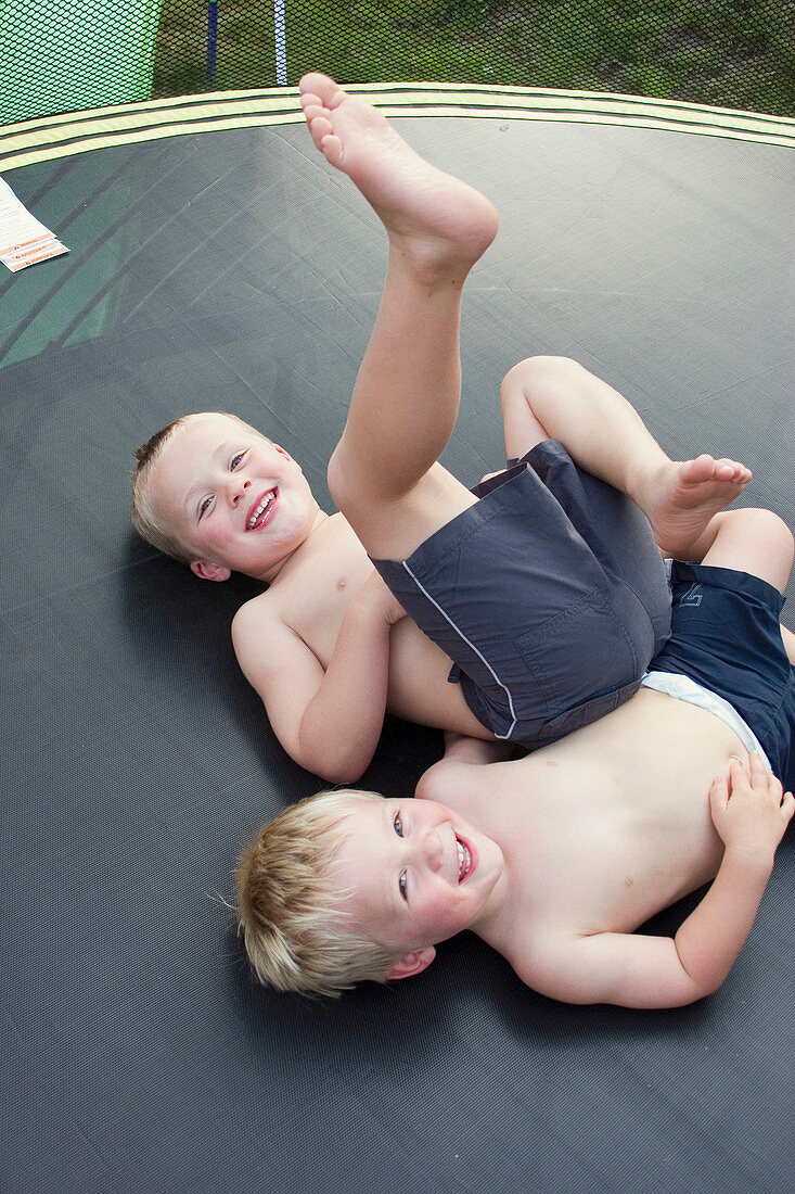 3 and 5 year old boys lying on their backs on a trampoline, laughing into camera