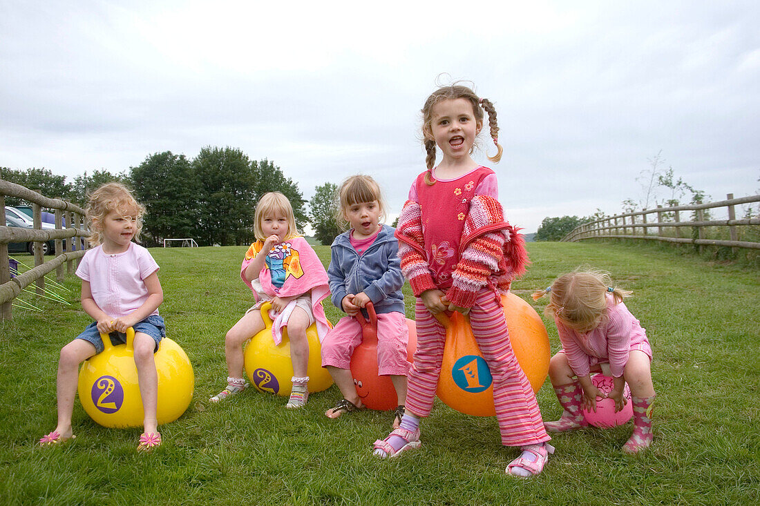 5 girs, aged 3-5 playing on bouncy hoppers, on a camping trip.