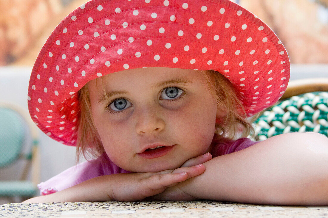 Beautiful 3 year old girl with huge blue eyes, smiling into camera, wearing a massive sunhat