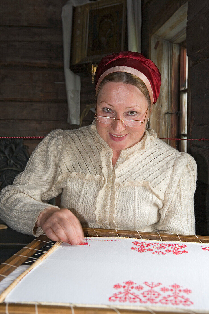 Frau in traditioneller karelischer Tracht stickt im Freilichtmuseum auf der Insel Kischi, Karalien, Russland