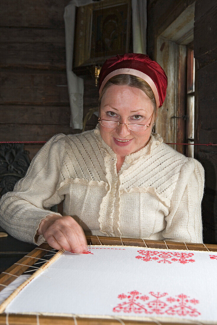 Woman in traditional Karelian dress doing embroidery in the open air museum on Kizhi island on Lake Onega, Karalia, Russia
