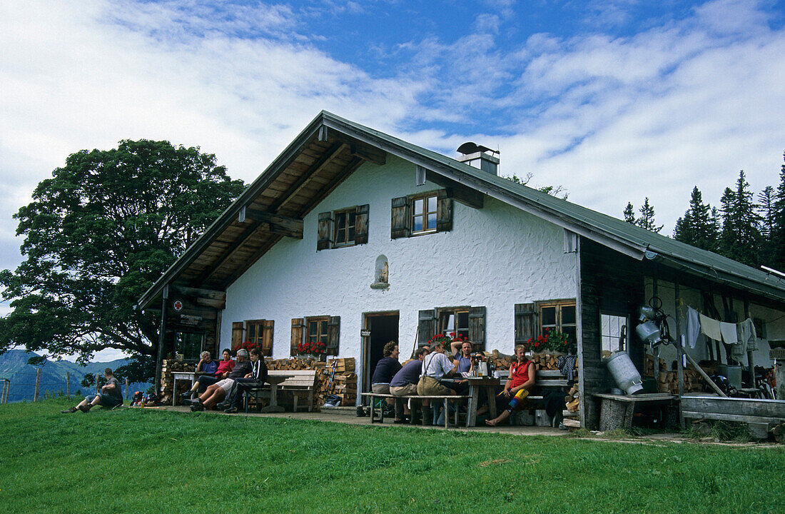 alpine hut Hofbauernalm with group of hikers on terrace, Kampenwand, Chiemgau range, Chiemgau, Bavarian foothills, Upper Bavaria, Bavaria, Germany