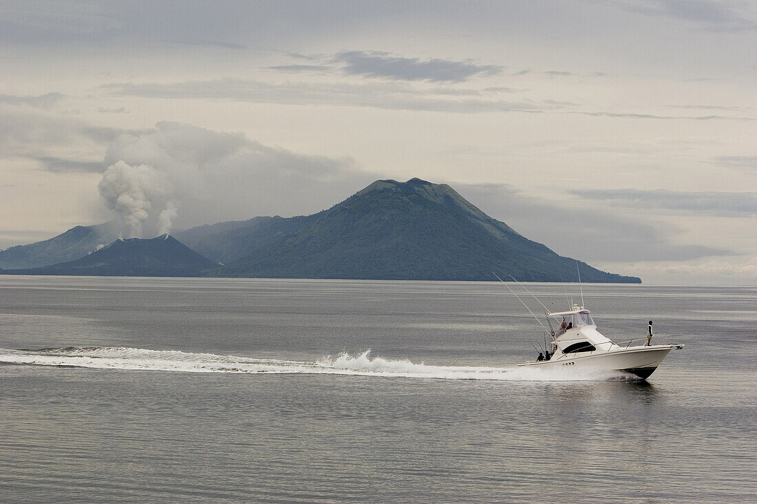 Motor boat in front of smoking volcano, Rabaul, New Britain, Papua New Guinea, Oceania