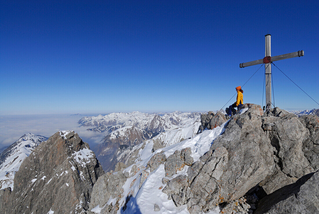 Woman sitting at summit cross of mount Madelegabel, Allgaeu Alps, Bavaria, Germany