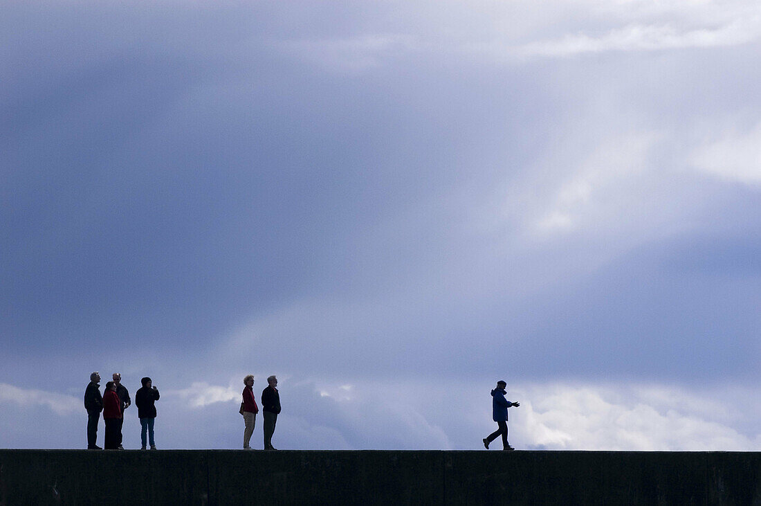 Human figures walking on Victoria breakwater sea wall. Victoria, BC, Canada