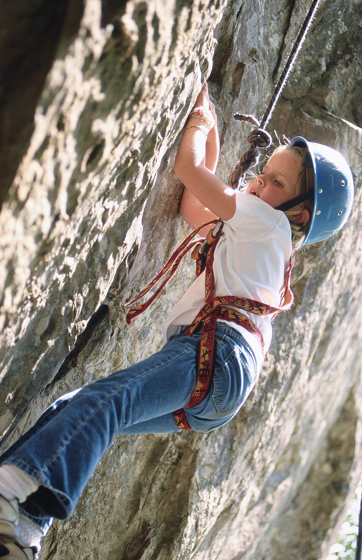 Young girl climbing rock face at rock climbing school