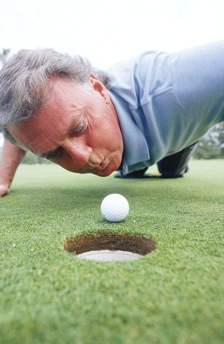 Frustrated man attempting to blow his golf ball into the hole