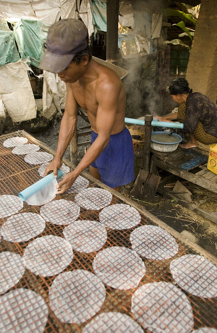 Man rolling out rice paper to dry as woman makes it. Don Teav, Battambang province. Cambodia.
