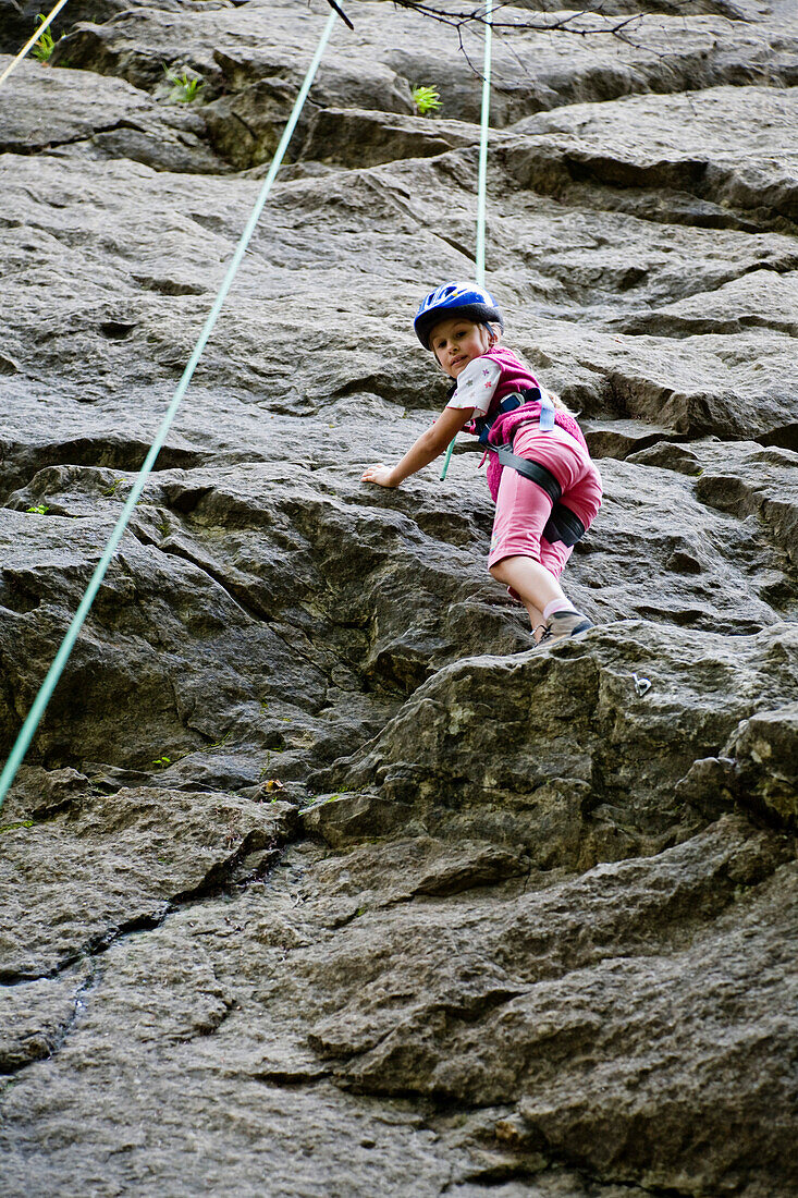 Mädchen (8-9 Jahre) klettert an einem Felsen, Oberbayern, Bayern, Deutschland
