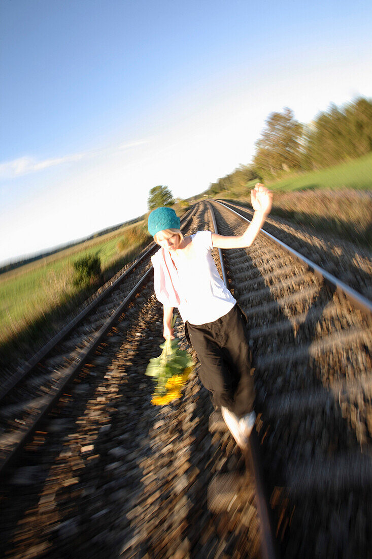 Young woman with sunflowers balancing on railway tracks, Kaufbeuren, Bavaria, Germany