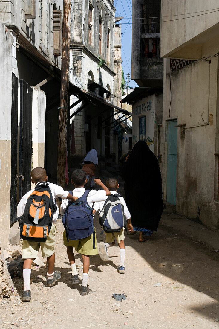 Three school boys walking through lane in Old Town, Mombasa, Kenya