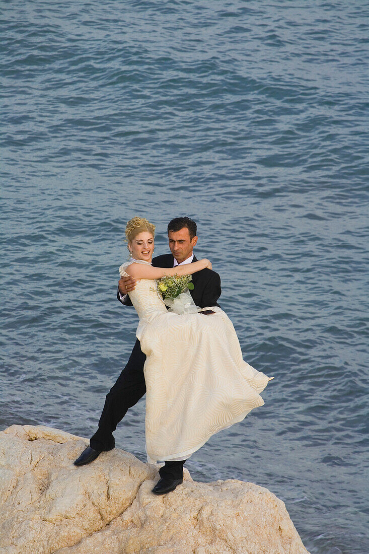Bride and groom, bridal couple on rocks at Petra tou Romiou, Rock of Aphrodite, Aphrodite's birthplace, Limassol, South Cyprus, Cyprus