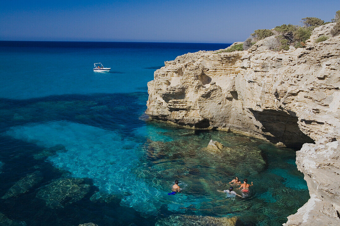 A group of young people bathing in the sea, coastal landscape with cave, boat, Akamas nature park, Cyprus