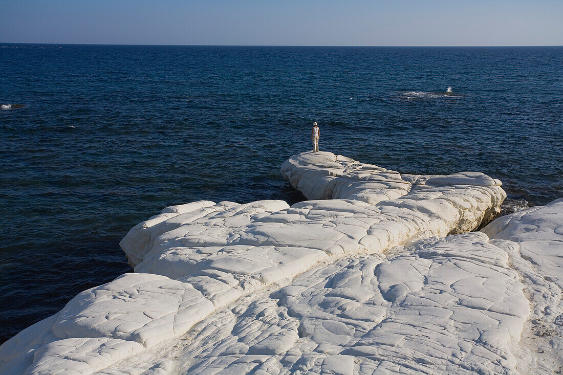 A woman standing on rocks looking out to sea, White rocks along the coast at Governors Beach, near Lemesos, near Limassol, South Cyprus, Cyprus
