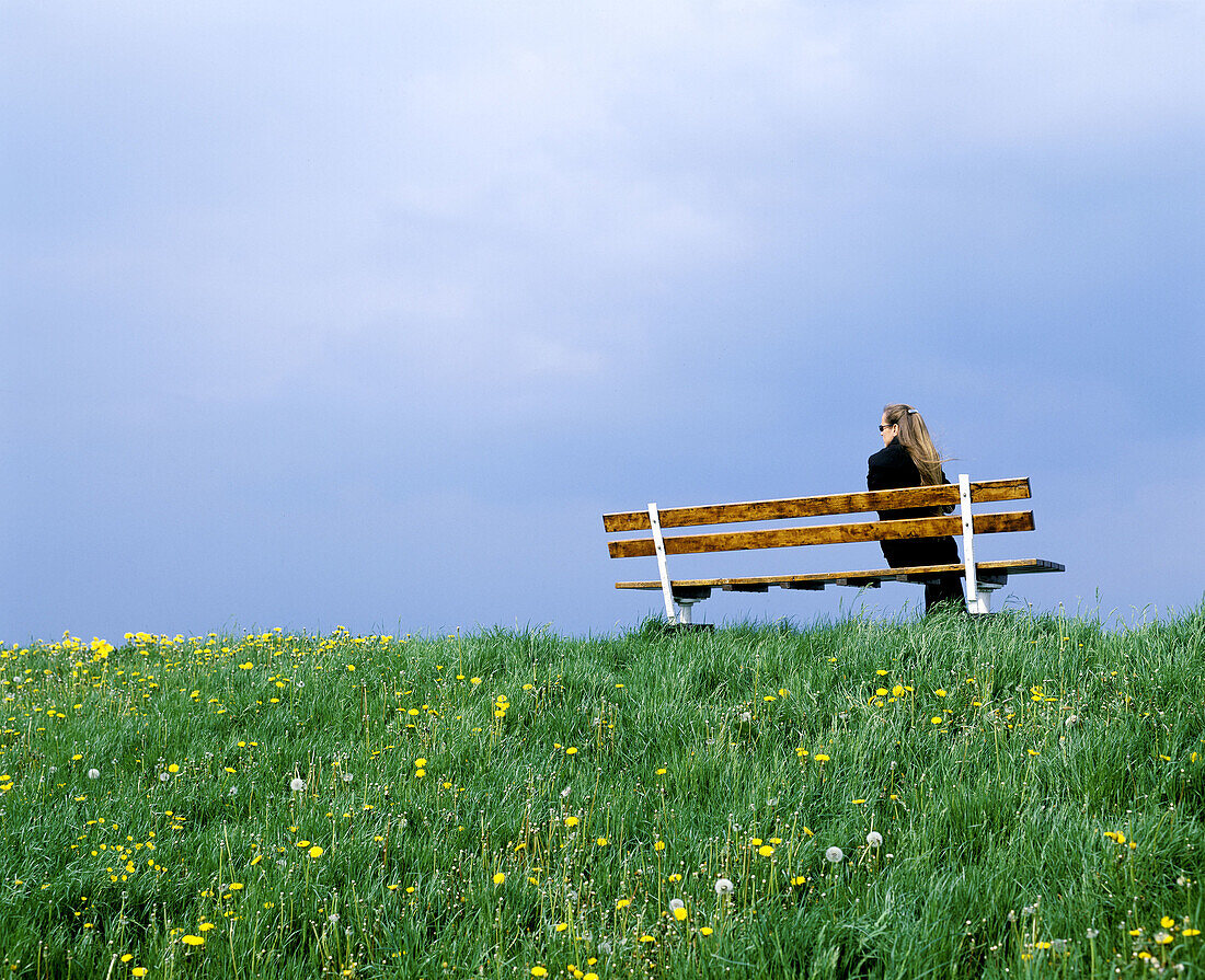 Woman sitting on bench during upcoming rain. Altes Land, Lower Saxonia. Germany