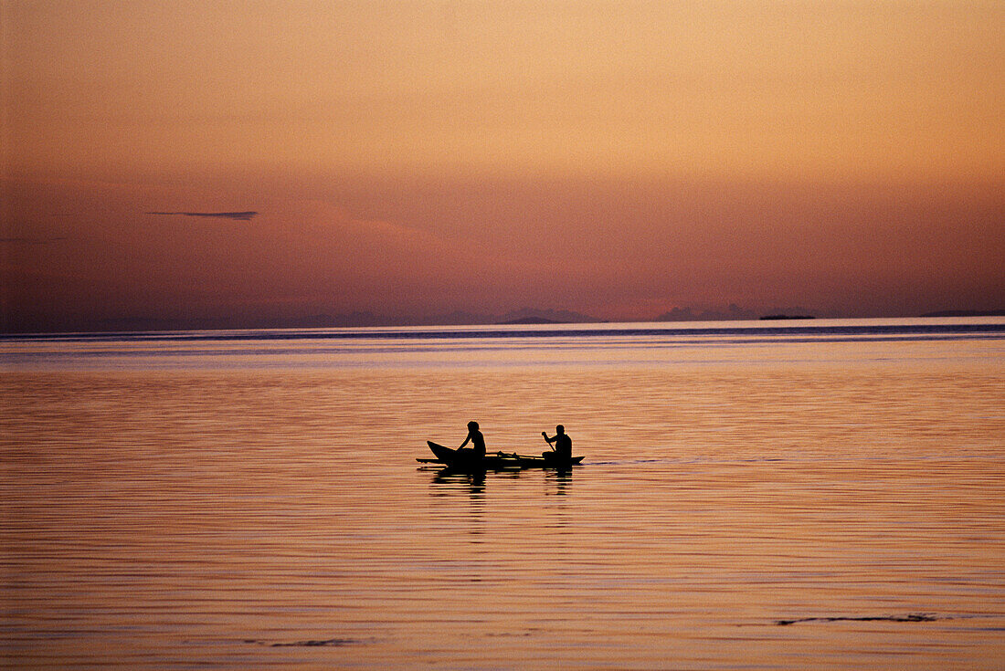 Two people rowing an outrigger canoe at sunset
