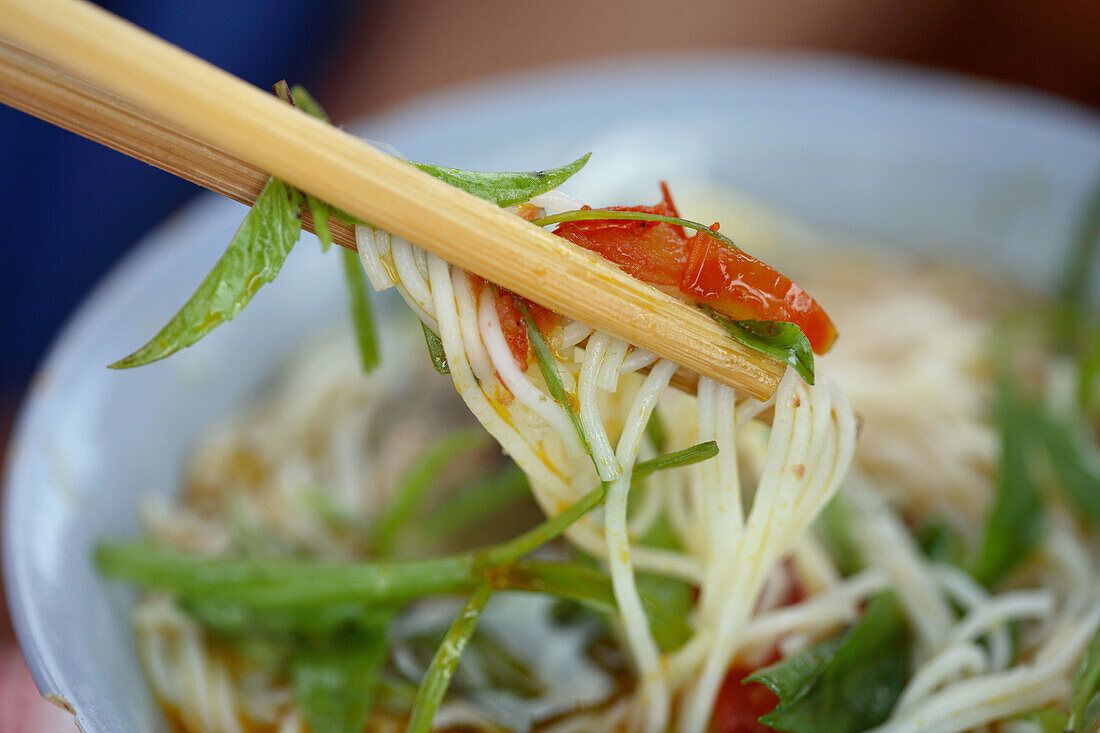 Eating noodle soup as a local speciality with chop sticks on the fresh food market of Hoi An, Vietnam, Southeast Asia