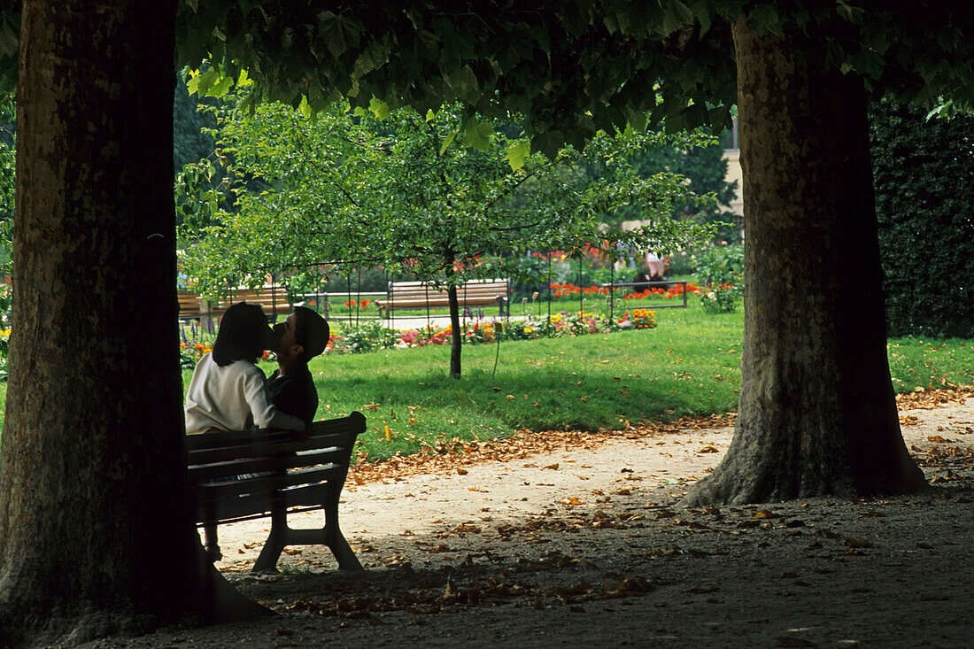 Kissing couple sitting on a park bench, summer, Paris, France