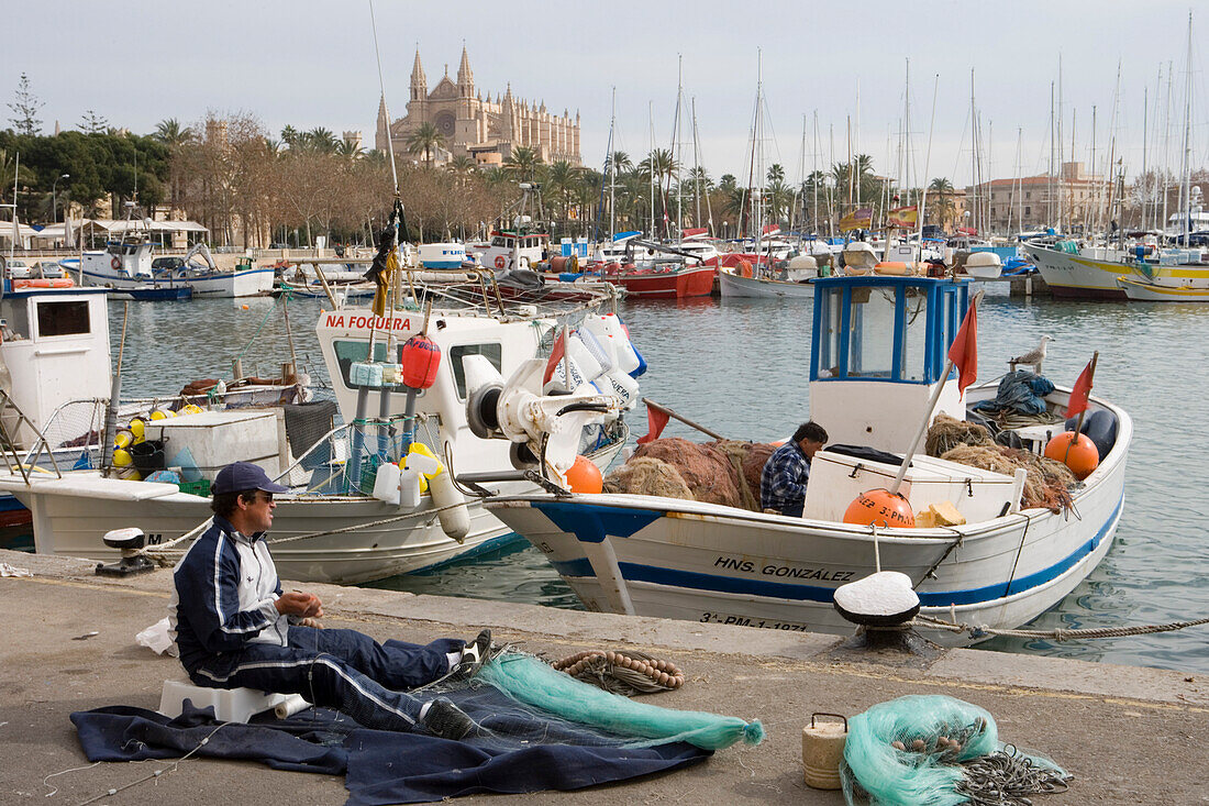 Fischer flickt Netze im Hafen mit La Seu Kathedrale im Hintergrund, Palma, Mallorca, Balearen, Spanien, Europa