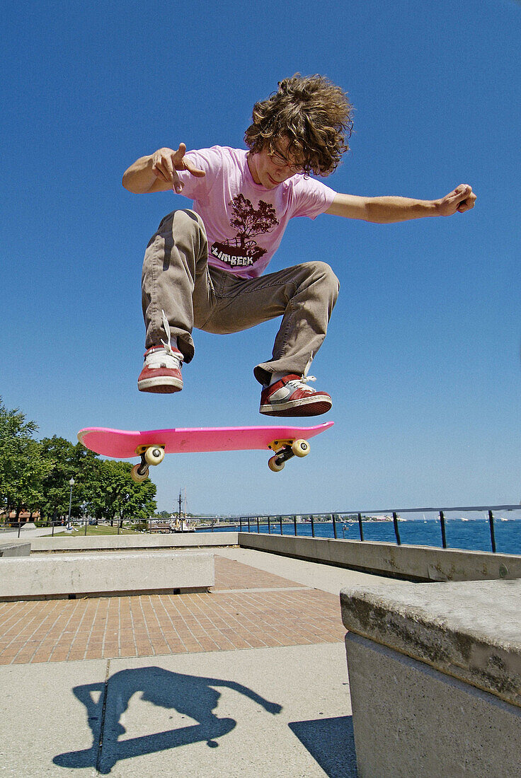 Teenage males perform jumping maneuvers on a skateboard in a public park