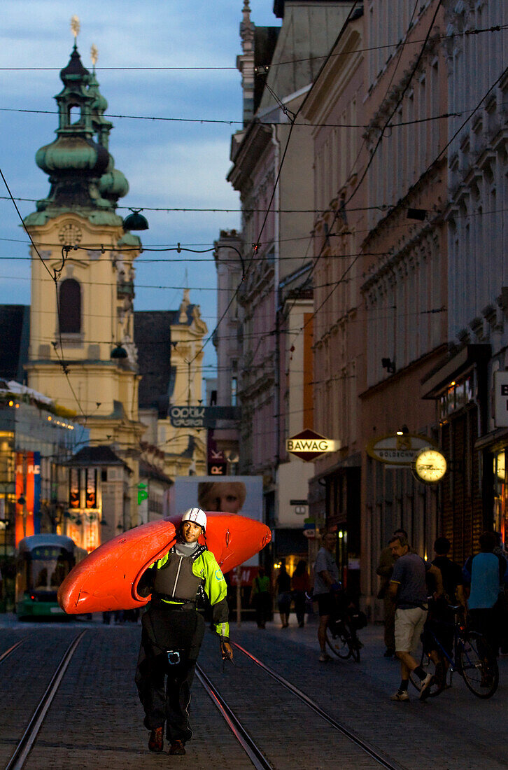 Mann trägt Kajak durchs abendliche Linz, Ursulinenkirche im Hintergrund, Oberösterreich, Österreich