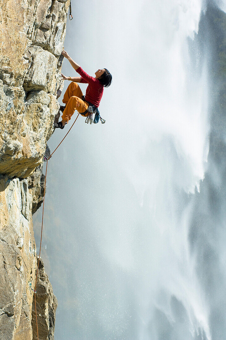 Freeclimberin klettert eine Felswand hoch, Gelber Wahn 7b+, Fallbachfall im Hintergrund, Maltatal, Nationalpark Hohe Tauern, Kärnten, Österreich
