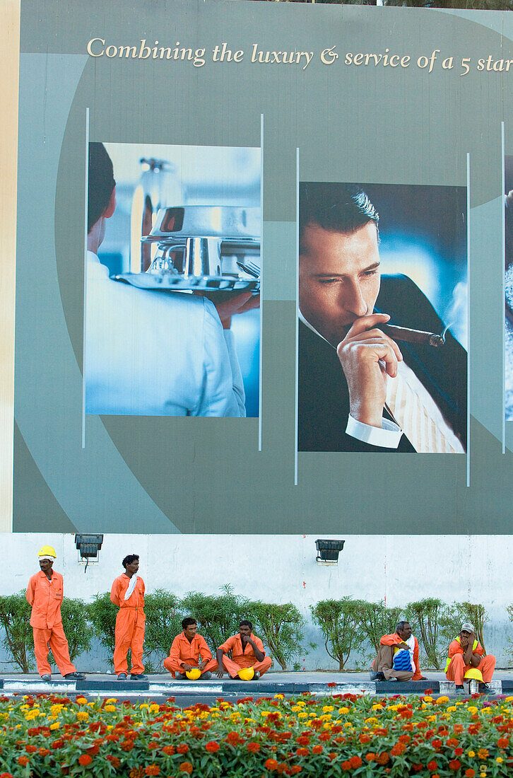Bauarbeiter rasten unter einem Werbeplakat für Luxus, Dubai, Vereinigte Arabische Emirate