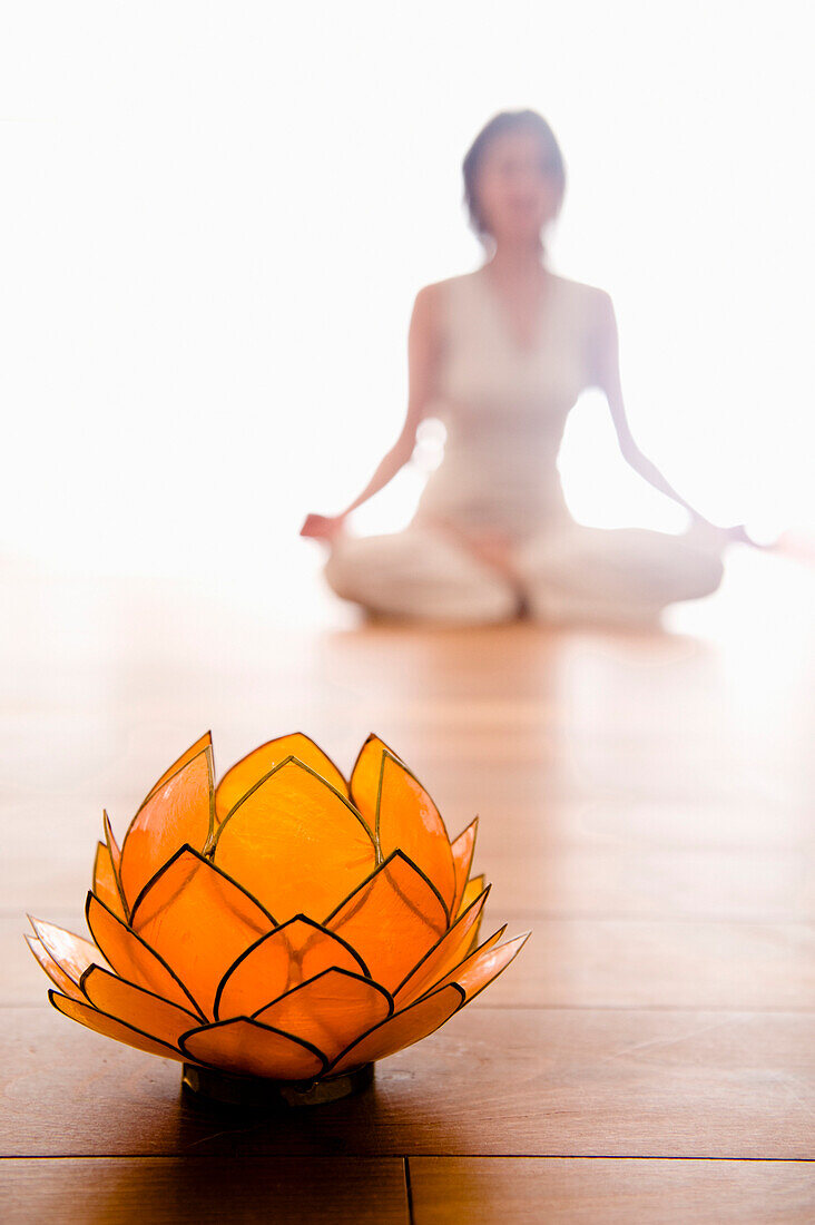 Frau mittleren Alters macht Yoga (Lotussitz), Lotosblüte im Vordergrund, Yogastudio in Linz, Österreich
