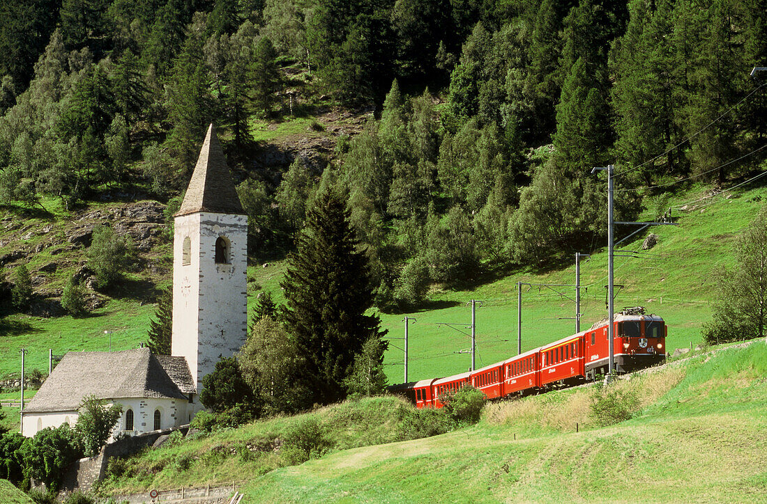 Rhaetian Railway train passing a church near Guarda, Grisons, Switzerland