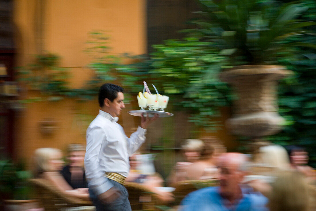 Kellner serviert Cocktails im Garten der Abaco Cocktail Bar in der Altstadt, Palma, Mallorca, Balearen, Spanien, Europa
